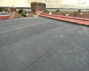 flat roofing materials on a residential building showcasing a chimney and neighboring rooftops while emphasizing three layers of roofing design