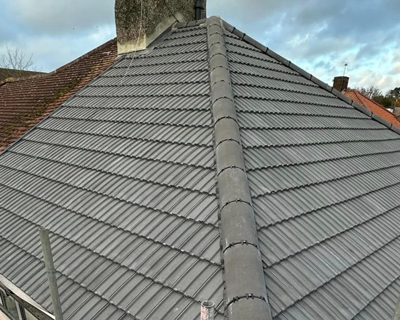 close-up view of a newly tiled roof with gray tiles and a chimney in the background featuring two distinct roof slopes and beautiful cloudy sky