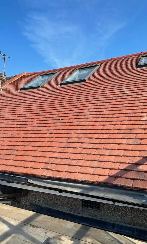 roof with red tiles and skylights under a clear blue sky showcasing eight distinct sections of roofing material