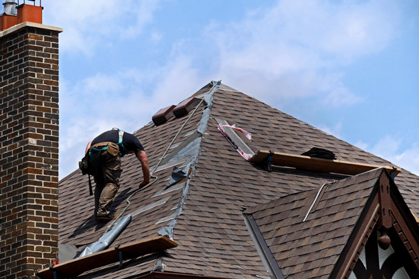roofer working on a steep roof with shingles and chimney under a blue sky depicting roofing repair techniques and safety considerations for home improvement projects