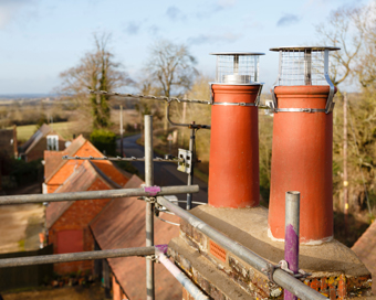 two brick chimneys on a rooftop with scaffolding in the background overlooking a rural landscape featuring trees and buildings close to ten unique structures