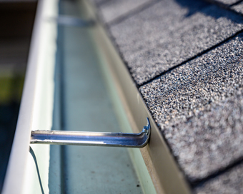gutter detail with roofing shingles showing a metal hook for secure fastening six gutter systems for maintenance